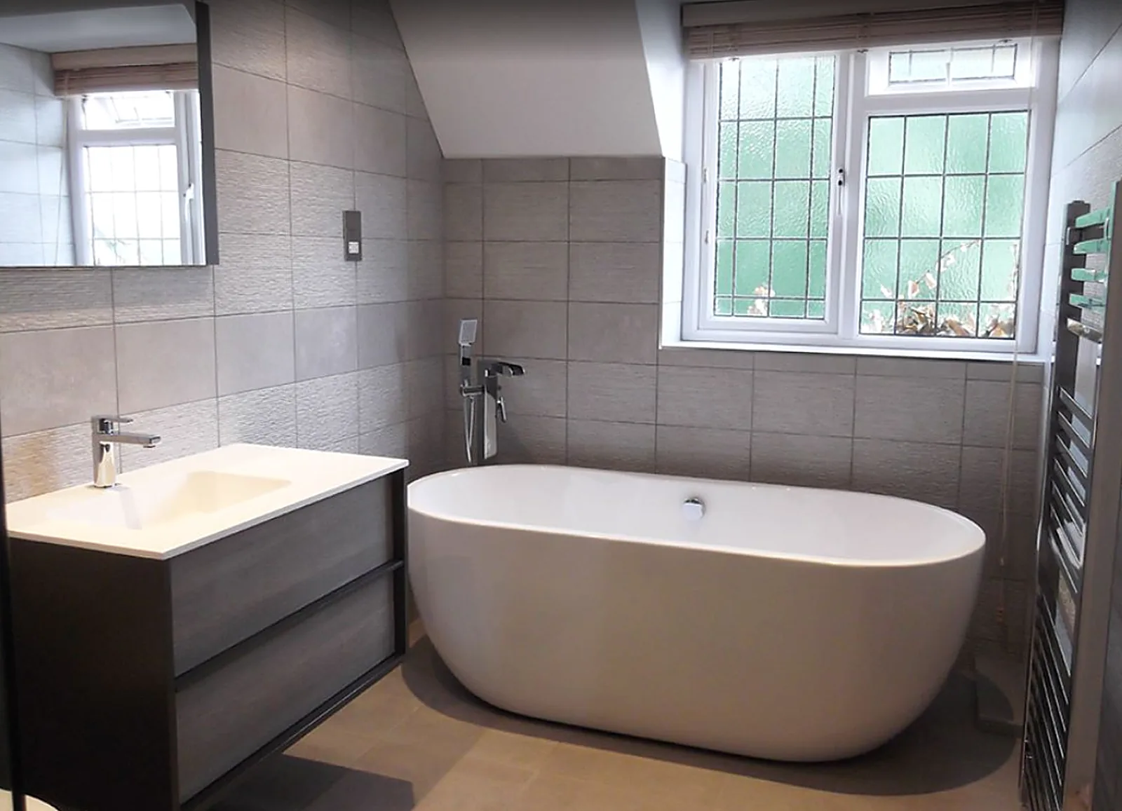 Finished bathroom with freestanding bath, vanity basin and chrome towel radiator by J&L Plumbing and Heating