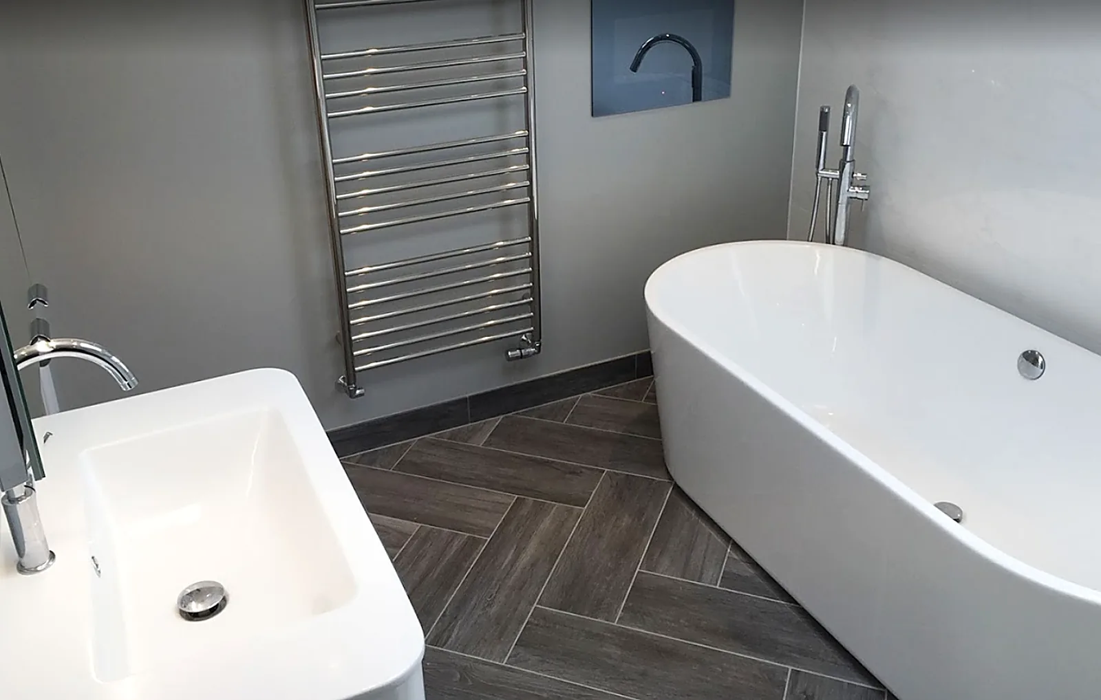 Freestanding bath, chrome towel radiator and herringbone floor tiles in a finished bathroom